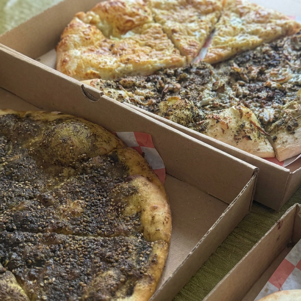 Several sliced Middle Eastern flatbreads in cardboard boxes, including za’atar and sesame-topped breads with assorted toppings.